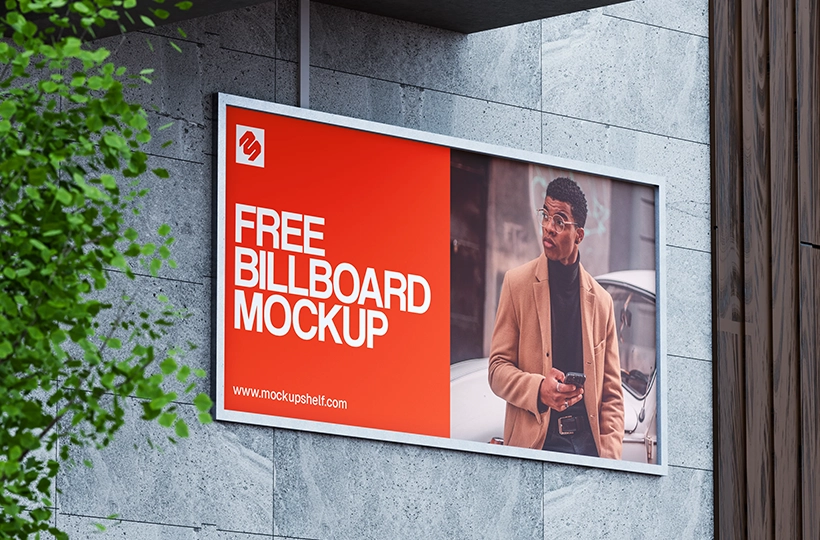 Free Street Billboard Mockup – side angled view on building wall with tree leaves | MockupShelf