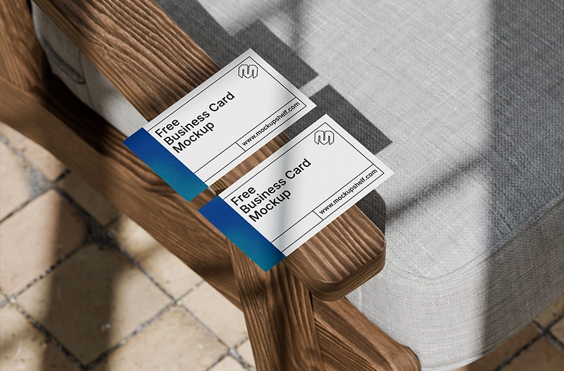 Two business cards placed on a wooden chair arm with soft natural light