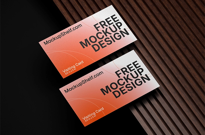 Two business cards placed on a brown wooden slatted surface with soft studio lighting