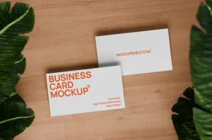 Free minimal business card mockup PSD — two white cards on light wood surface with tropical monstera leaves