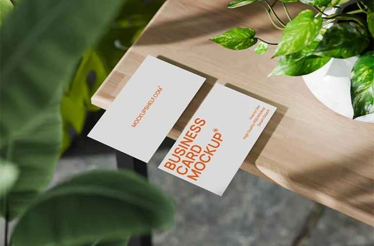 Free minimal business card mockup PSD — two white cards on warm wooden desk with tropical plants